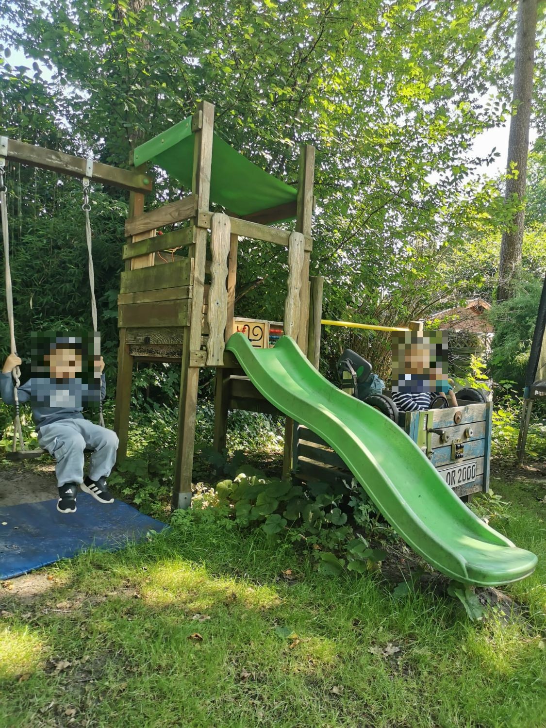 Kinder schaukeln und sitzen am Spielturm im Garten